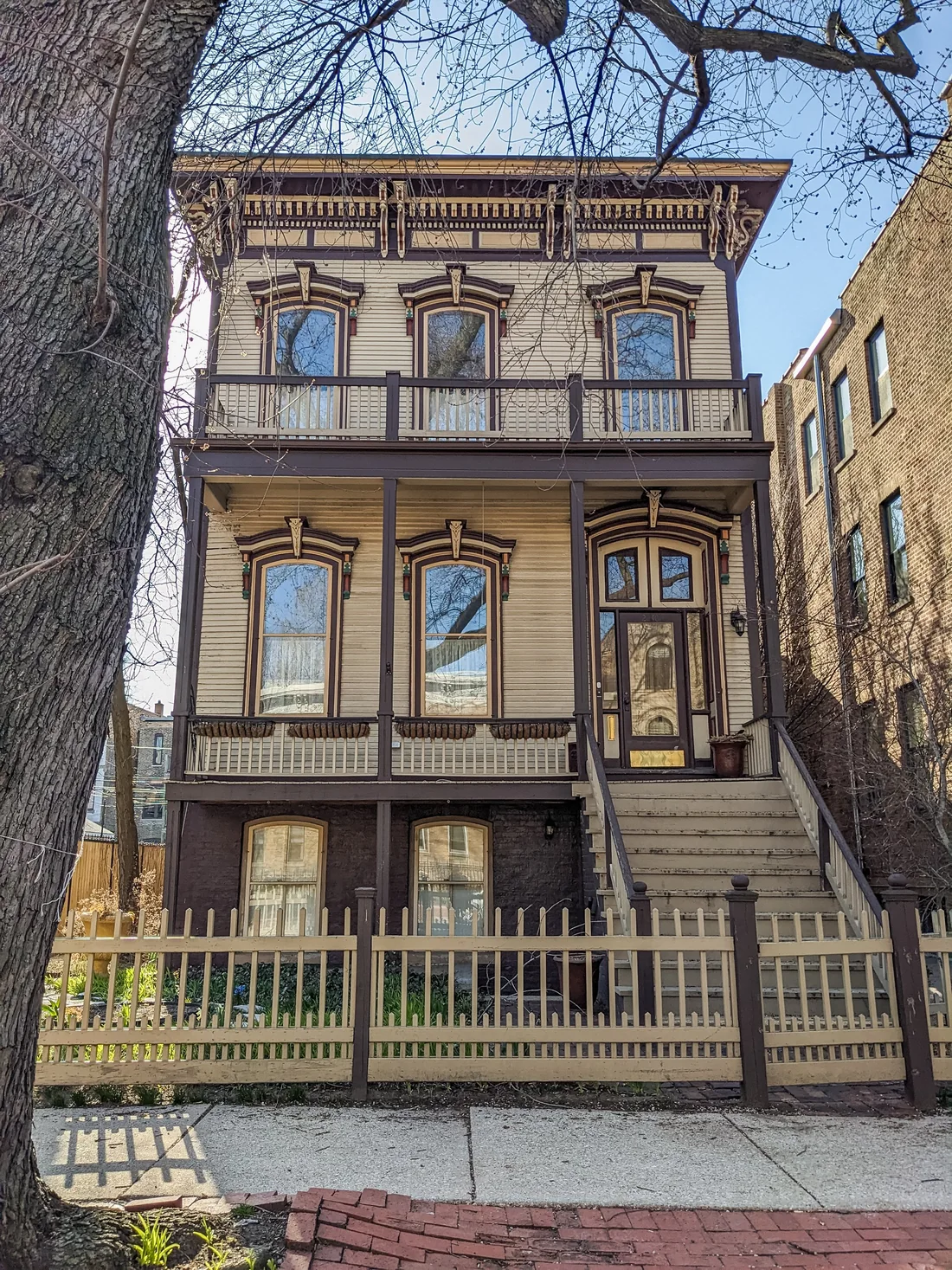 2240 N. Burling Street: a three-story Italianate wood frame three-flat, cream with dark brown trim, bracketed hoods over tall windows, a two-story front porch and an ornate bracketed cornice